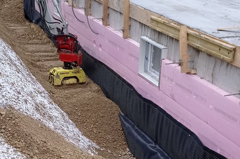 Concrete basement wall with insulation boards and dimpled drainage membrane